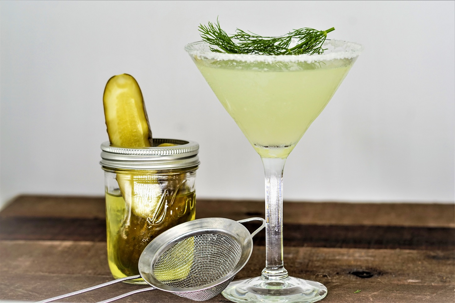 Dill Pickle Martini with jar of pickles and cocktail strainer